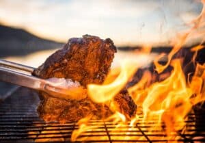 A t-bone steak being char-grilled over open flames on a commercial gas grill