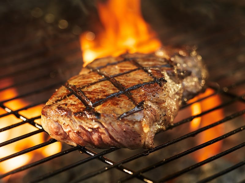 Steak cooking over flaming grill